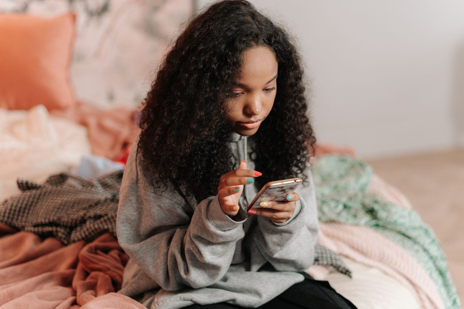 A teenager sitting on a bed using a phone, the setting where ChatGPT for Teens now applies by default