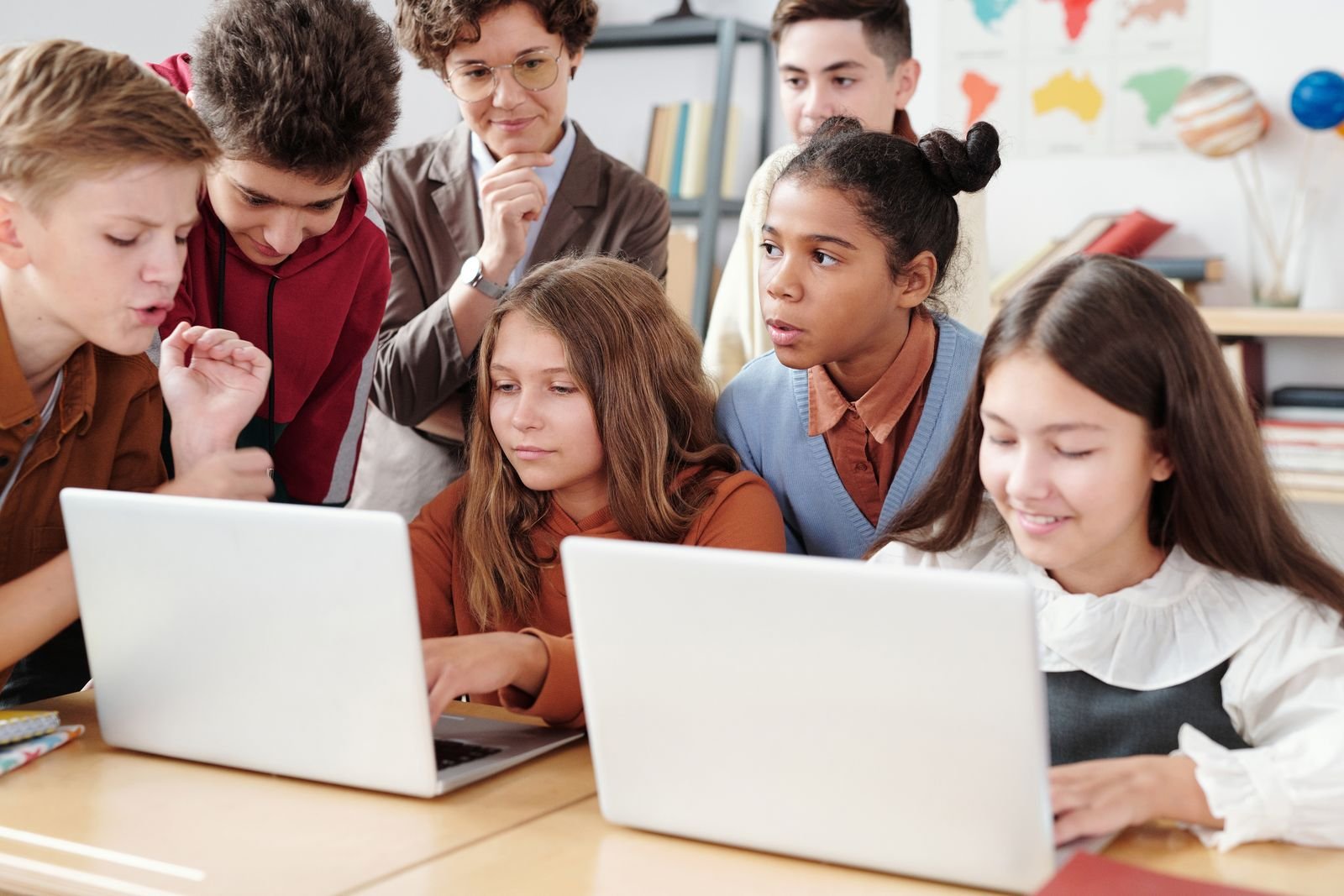 A group of middle school students gathered around two laptops in a classroom