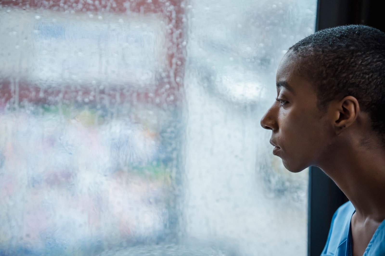 A young person sitting by a rain-covered window looking away, the kind of heavy chatbot use ChatGPT for Teens break reminders target