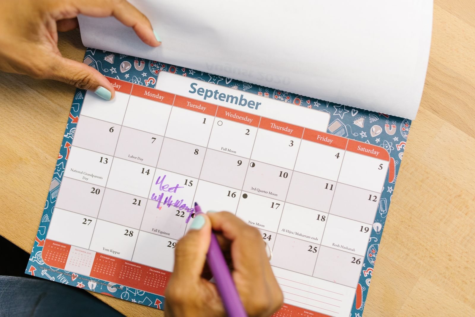 A hand marking a September date on a desk calendar, one busy month picked out of the year