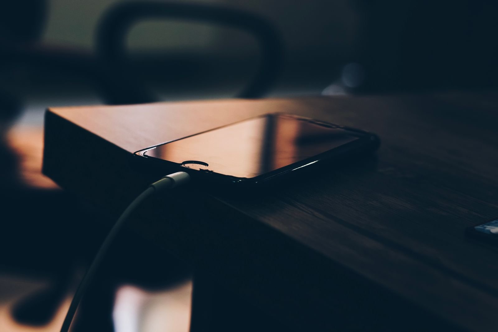 Phone plugged into a charger on a dark wooden desk