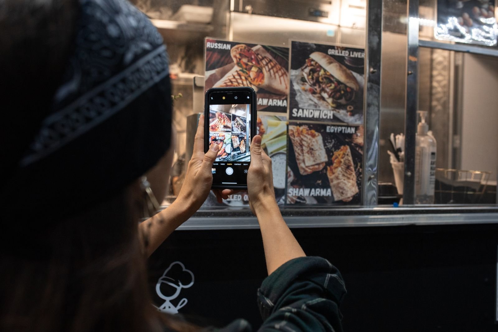 A traveler pointing a phone camera at a street food menu at night