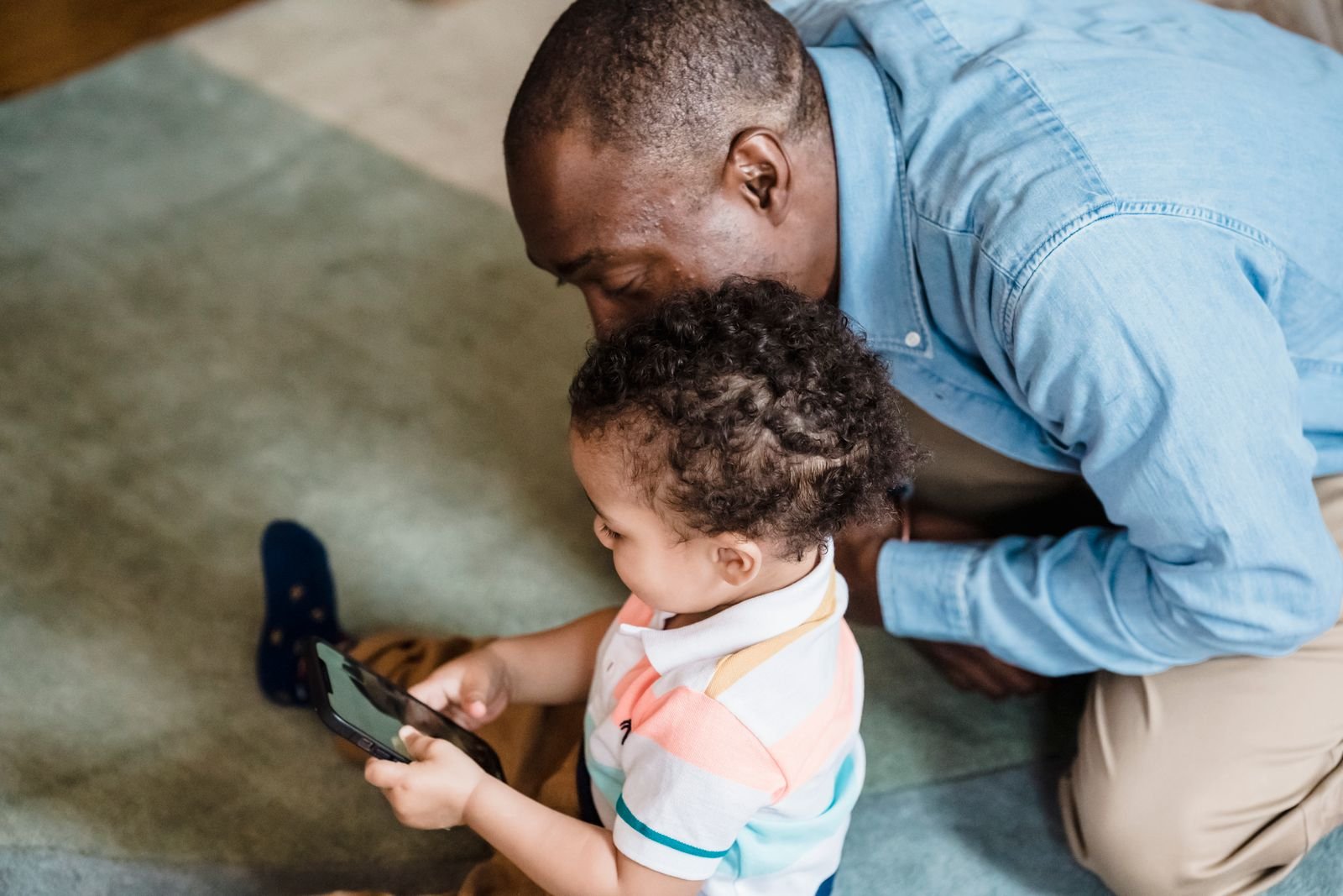A father and son looking at a smartphone together on the couch, like a parent setting Screen Time limits for Siri